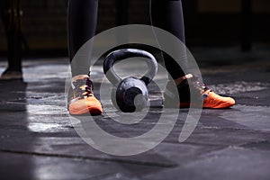Cropped image of young woman, legs in the black leggings, orange sneakers and kettlebell. Crossfit workout