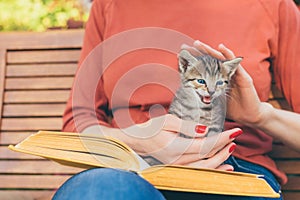 Cropped image of young woman sitting in the garden with book and tabby kitten