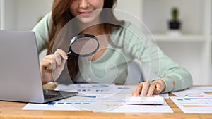 Cropped imaged of female auditor inspecting financial document with a magnifying glass at office desk