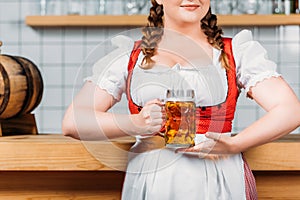 cropped imageo of oktoberfest bartender in traditional bavarian dress holding mug of light beer