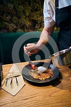 Cropped male chef adding kiwis and cherries in jam to frying waffle on plate