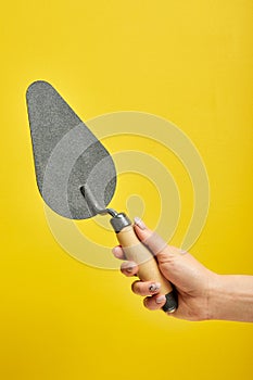 cropped male holding spatula in hands, for cleaning a concrete wall from defects, repair and construction
