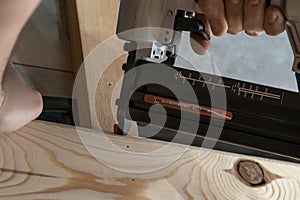 Cropped man hands using pneumatic construction stapler, pistol nail gun for wooden plank. Hammer replacement technology