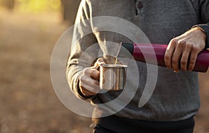 Cropped of man pouring hot tea from thermos in forest