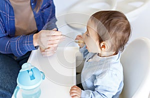 cropped mother feed little toddler baby boy with baby food, from plastic spoon in high chair front view. Motherhood