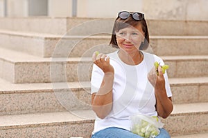 cropped photo of adult woman on stairs and eating grapes on summer warm day. female in casual clothes eating fresh green