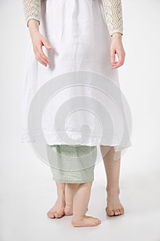 Cropped photo of barefoot family standing on white background. Unrecognizable woman hiding little girl under dress.
