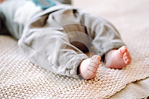 Cropped photo of barefoot infant newborn lying on beige cotton knitted plaid. Close-up of cute tiny baby feet on bed.