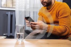 Cropped photo of a beard adult man, dependent of virtual world. Online psychotherapy session, a glass of water on the table. A photo