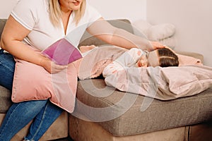 Cropped photo of caring mother holding a pink book and reading for her little girl and putting her hand on her daughter