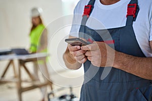 Cropped photo of construction worker typing message on phone