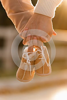 Cropped photo of couple, man and pregnant wife are holding hands and warm baby shoes on nature autumn background