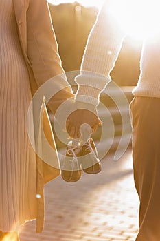 Cropped photo of couple, man and pregnant wife are holding hands and warm baby shoes on nature autumn background