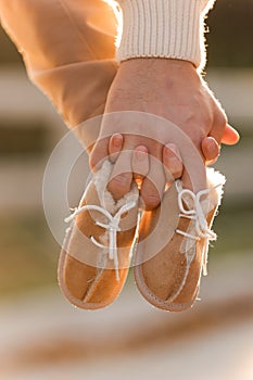 Cropped photo of couple, man and pregnant wife are holding hands and warm baby shoes on nature autumn background