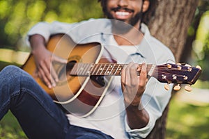 Cropped photo of dark skin young man hold play guitar music lover sit in park outside in outdoors