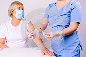 Cropped photo. A doctor in disposable latex gloves holds out an ampoule with covid 19 vaccine and a syringe to the