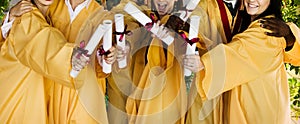 Cropped photo of excited young students showing diplomas on graduation day in college