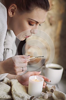 Cropped photo of female hands with lit match lighting candle on windowsill, hygge lifestyle
