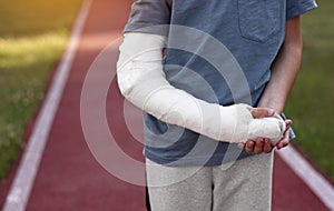 cropped photo of little boy with broken hand outdoors on sports ground on summer day. 9 years child with a fractured