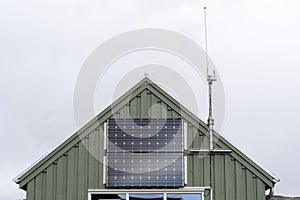 Cropped photo of little green house with small solar panel at the front of the building next to the cellular antenna against gray