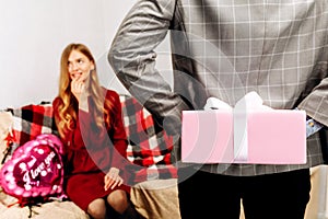 Cropped photo of male hands hiding while holding gift box with ribbon behind back  happy woman on blurred background  celebrating