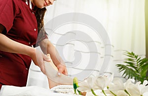 Cropped photo of a masseur spacialist in red uniform making feet massage procedure to a client woman in spa salon.