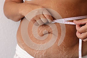 Cropped photo of naked overweight woman belly in underwear, trying to lose weight. Holding and measuring her waistline