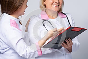 Cropped photo of senior doctor with stethoscope near young medical resident in white coat, showing medical information, diagnosis