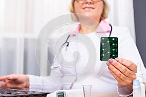 Cropped photo of senior female doctor holding pill blister to camera. Doctor talking with patient to inform about medication