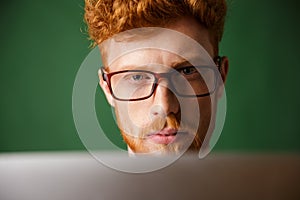 Cropped photo of serious young readhead man in glasses, working