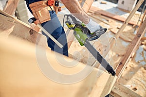 Experienced builder cutting construction wood with chainsaw