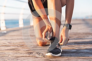 Cropped photo of slim european sportswoman 20s in tracksuit squatting, and tying his sneaker laces during workout on boardwalk