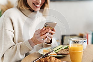 Cropped photo of smiling woman using cellphone while having breakfast