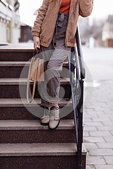 Cropped photo of a stylish young woman holding beige handbag on the stairs