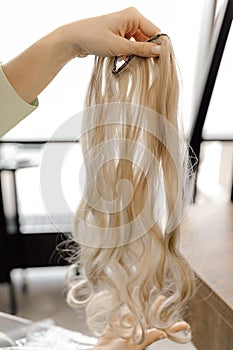 Cropped photo of woman hairdresser holding long fair blond hairpiece chignon weave bundle for extension in beauty salon. photo
