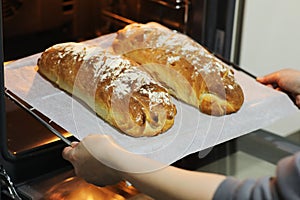 Cropped photo of womans hands take out hot fresh baked breads from an electric oven on metal tray in the kitchen at home