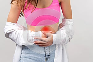 Cropped photo of a young girl in teenege clothes having stomach ache holding it with two hands, health care concept.