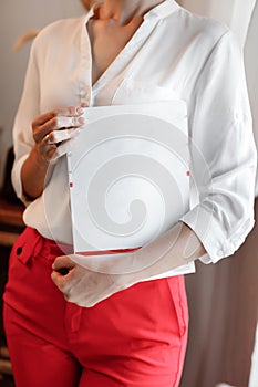 cropped photo of young woman holding a magazine with mock up. girl in a white shirt and red pants standing near the