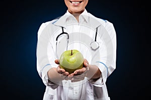Cropped photo of young woman in medical gown holding green apple