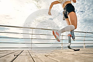 Cropped photo of a young woman with a prosthetic leg running on the bridge. Female sportsperson training outdoors photo