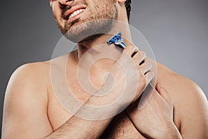 Cropped picture of naked man smiling and shaving his neck with r