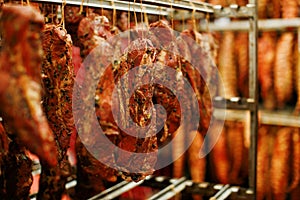 Cropped picture of a pieces of smoked spicy meat, hung on hooks and arranged on a stand