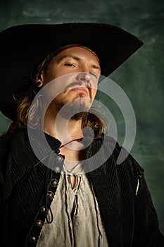 Cropped portrait of brutal man, medeival pirate in hat  over dark background.