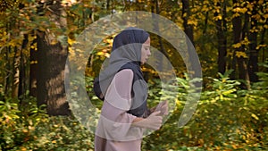 Cropped portrait in profile, dolly shot of young Muslim girl in hijab running in autumnal forest.