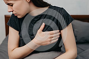 Cropped portrait of sad worried girl suffers from heartache sitting on bed at home