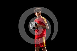 Cropped portrait of young boy, teenager, professional football player in uniform with ball posing isolated over white