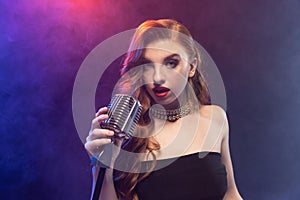 Cropped portrait of young female jazz singer isolated over gradient blue purple background in neon light with stage