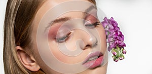Cropped portrait of young girl with closed eyes, bright makeup, purple flowers curled in hair. Health and natural beauty