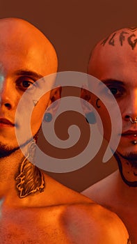 Cropped portrait of young half naked twin brothers with tattoos and piercings looking at camera, posing together