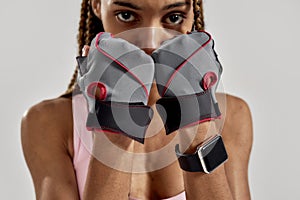 Cropped portrait of young sportive mixed race woman in sportswear looking at camera, wearing fitness gloves while posing